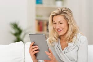 Mature woman reading about facelift vs. filler on a tablet.