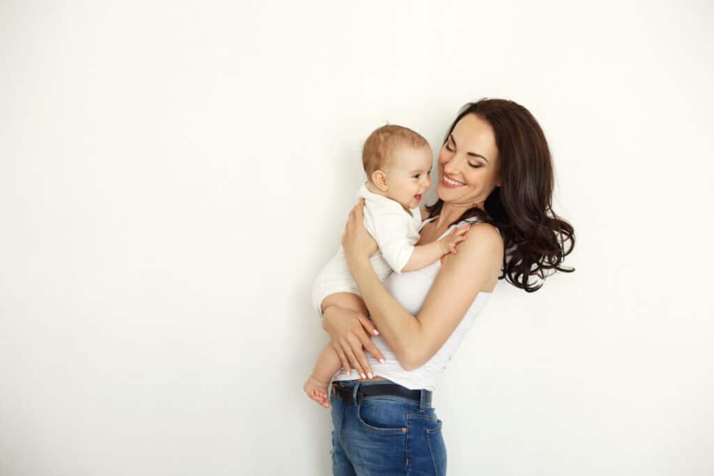 Slim, toned mom holding baby after her mommy makeover with liposuction in Louisville, KY